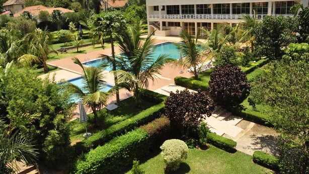 A pool surrounded by lush greenery, a building with large windows, and a well-maintained garden. - Hotel Brovad Masaka (Masaka)