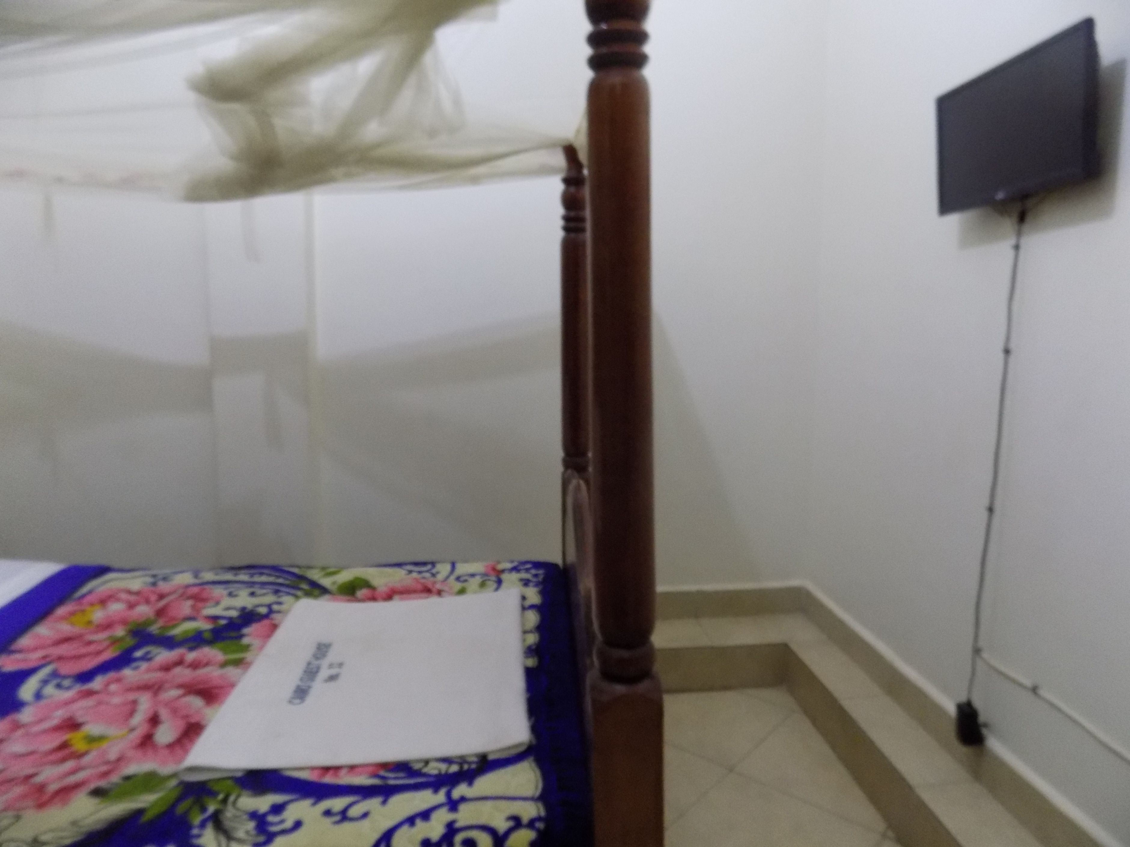 A bedroom with a wooden bed frame, a floral bedspread, and a flat-screen TV mounted on the wall.