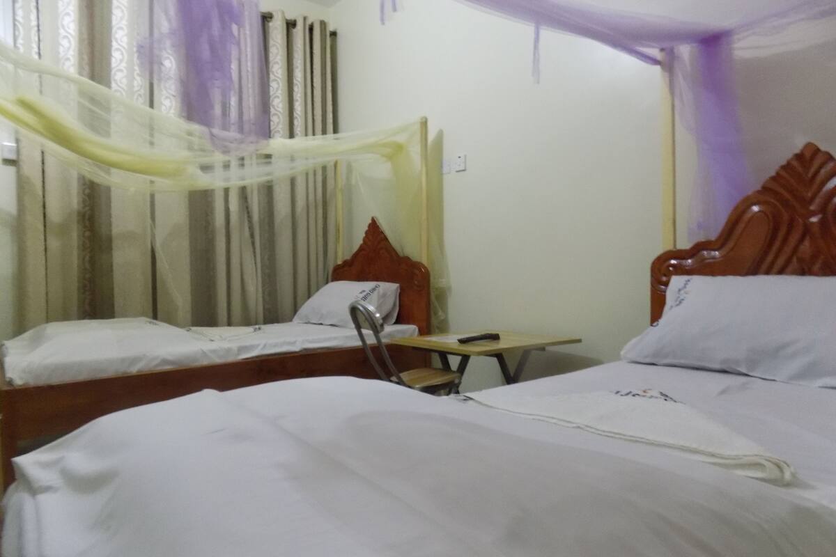 Une chambre d’hôtel avec deux lits, une table de chevet et un rideau.
