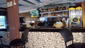 A bar area with a tiled wall, a television mounted on the wall, and shelves stocked with bottles. - Japs Motel Mbarara (Mbarara)