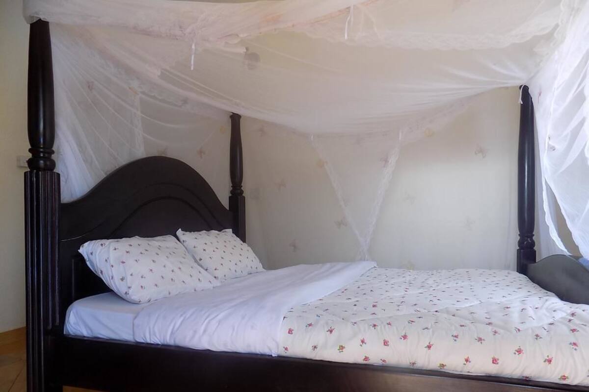 A four-poster bed with a canopy, white bedding, and floral-patterned pillows.