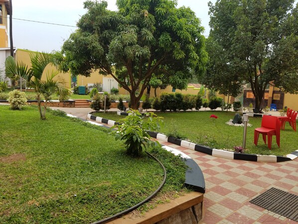Une cour avec un chemin pavé, de l’herbe verte et une variété d’arbres et d’arbustes.