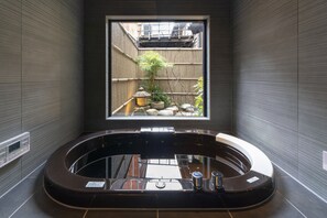Ein modernes Badezimmer mit einer großen Badewanne, einem Fenster mit Blick auf einen Bambusgarten und einer Wandbedienung.