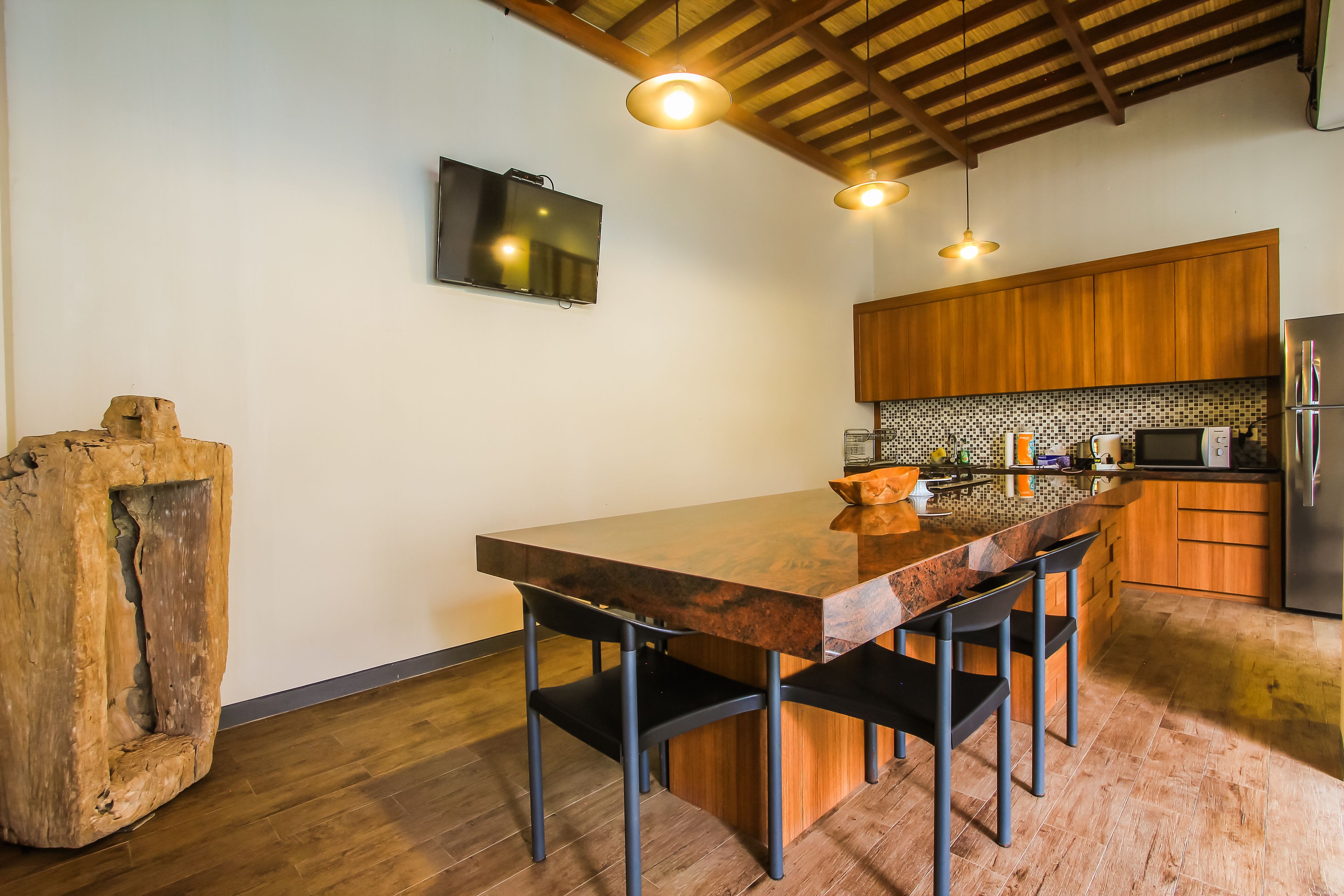 A modern kitchen with a wooden island, bar stools, a TV mounted on the wall, and a built-in microwave.