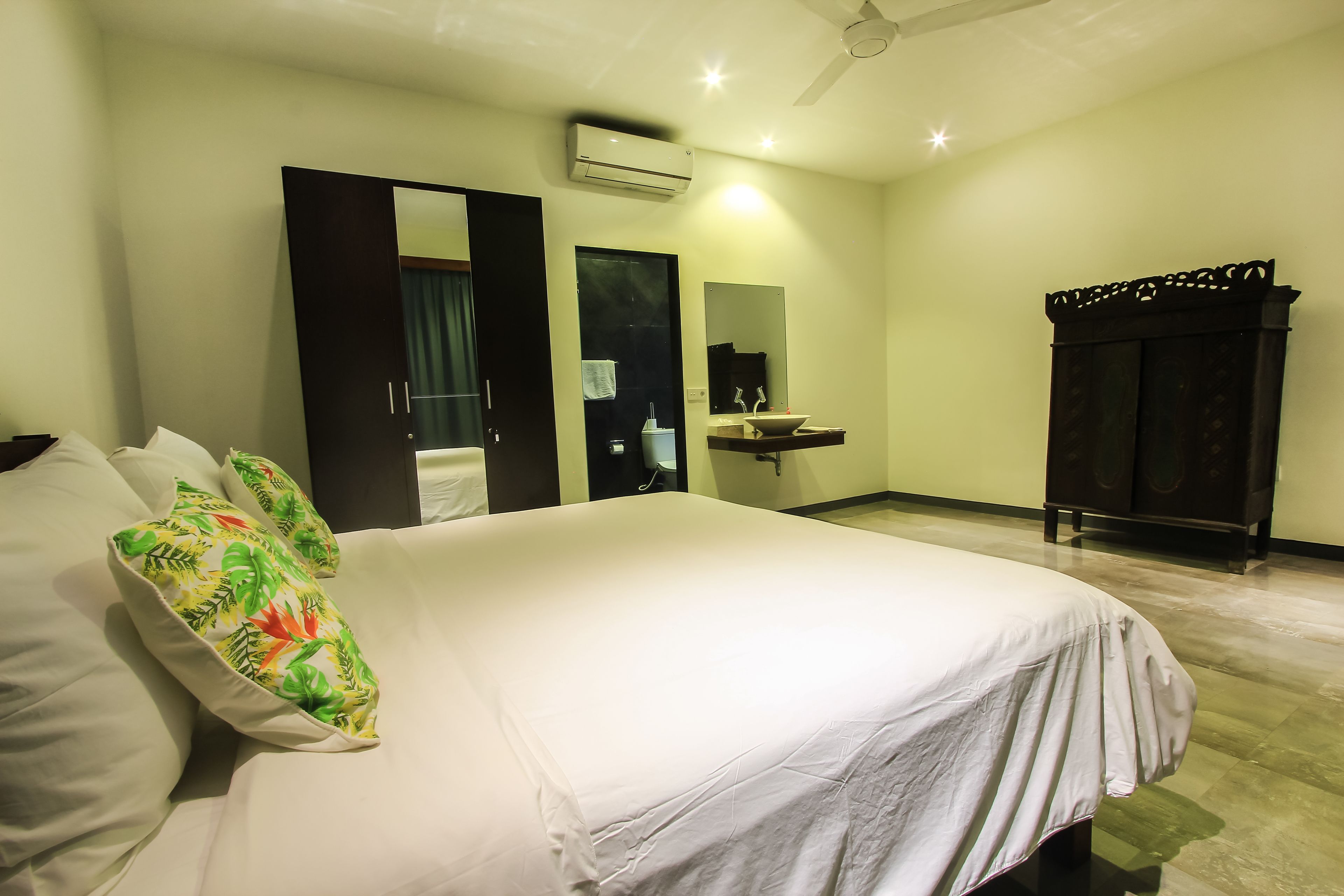 Une chambre à coucher comprenant un lit, une table de chevet, un miroir, une armoire et une salle de bain avec un lavabo et un miroir.