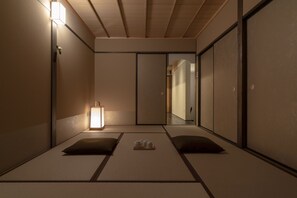 A traditional Japanese room with tatami flooring, a shoji screen door, and a small bedside table with a lamp. - Mimari (Kanazawa)