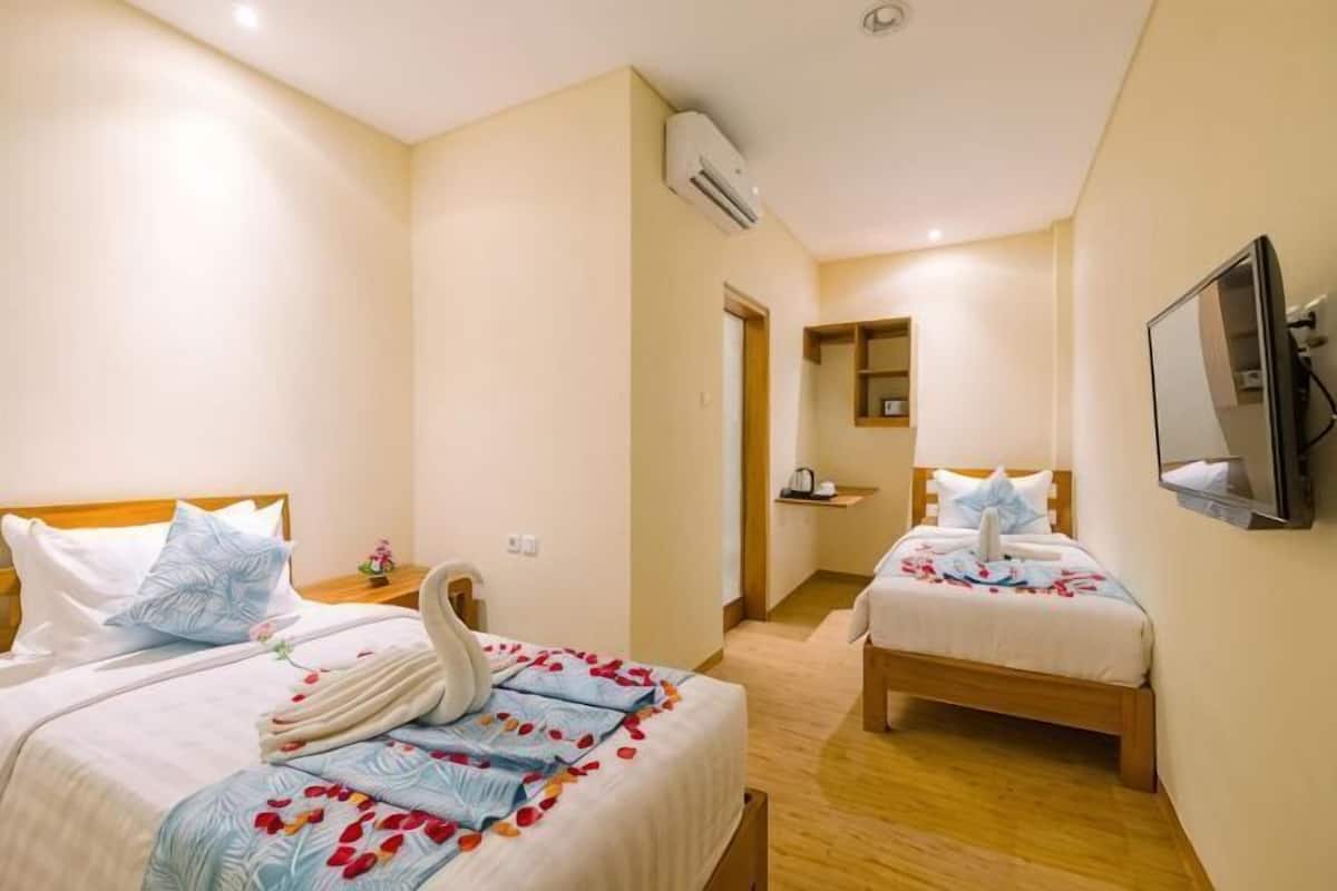 Quarto de hotel com duas camas, televisão, aparelho de ar condicionado e banheiro pequeno.