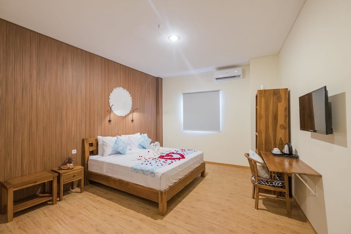 Quarto com cama de madeira, mesas de cabeceira, escrivaninha, cadeira, televisão e janela.