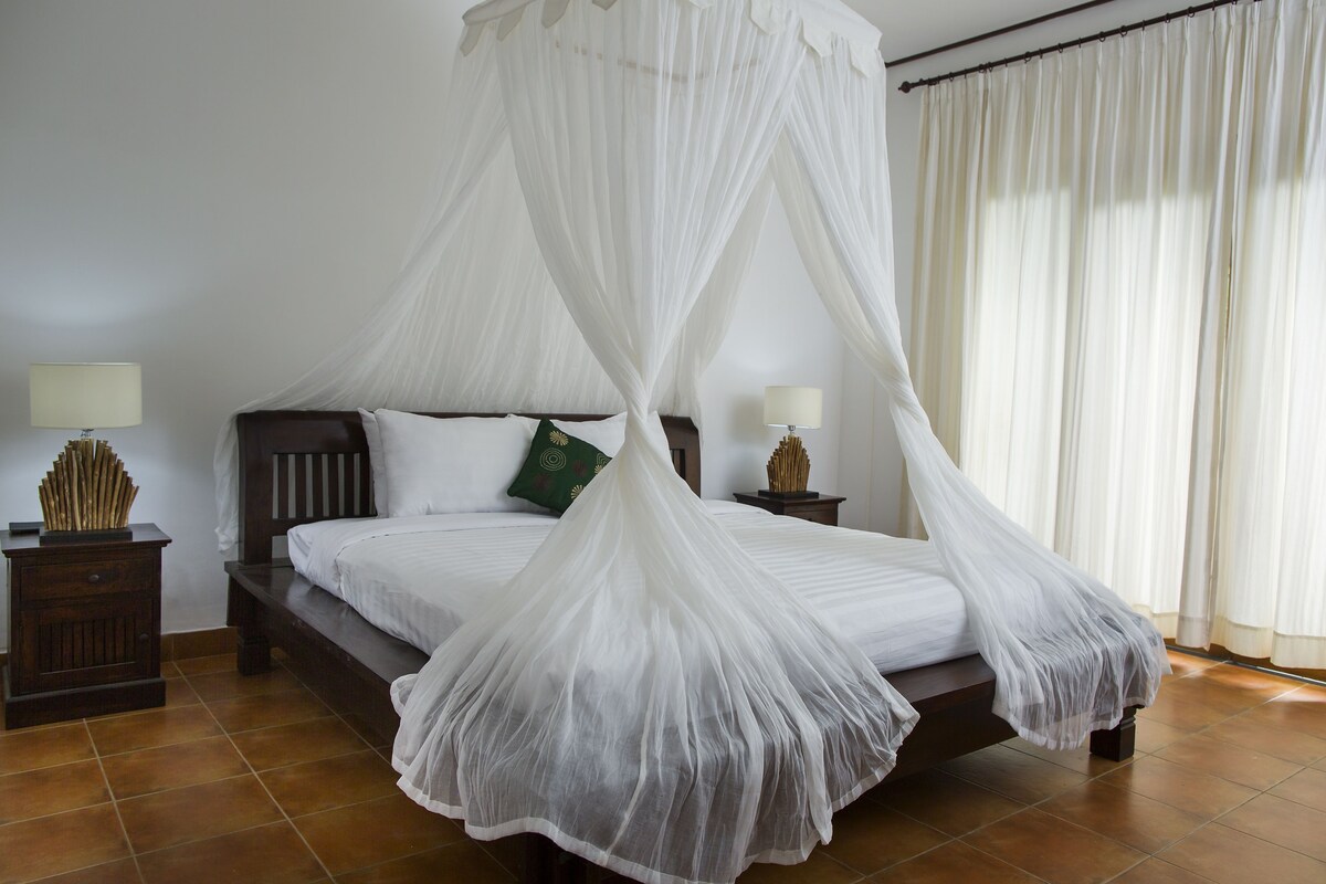 Une chambre à coucher avec un lit à baldaquin, une table de chevet avec une lampe et une petite table de nuit agrémentée d’un objet décoratif.