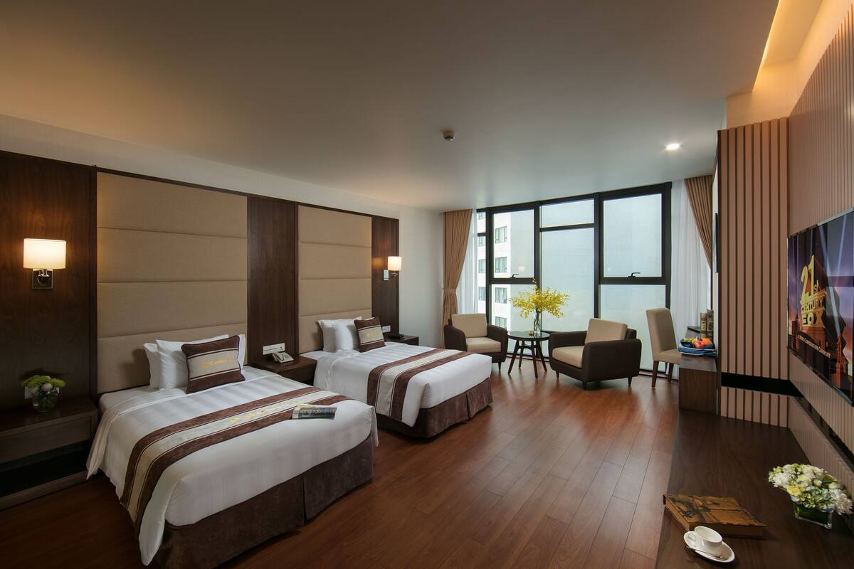 A hotel room with two beds, a sitting area with a table and chairs, and a large window providing a view.