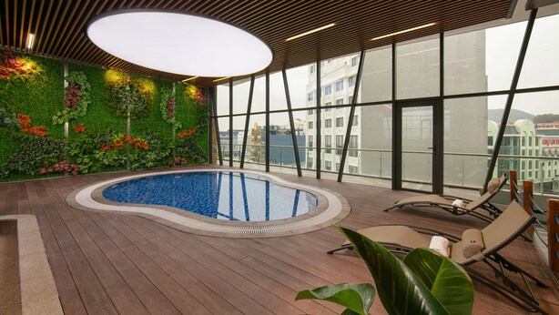 Piscina interna con bordo in legno, circondata da ampie finestre e una parete verde con piante.