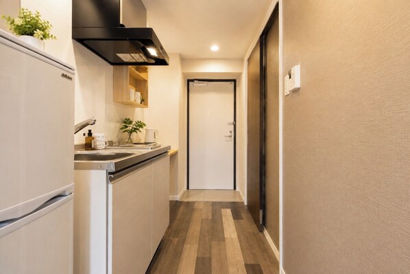 Un pasillo estrecho con una zona de cocina a un lado, una puerta al final y un termostato en la pared.