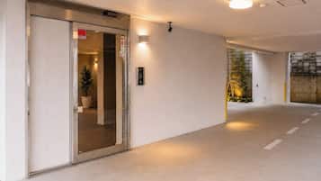 Un couloir avec une porte d’entrée en verre, un luminaire fixé au mur et une plante en pot.