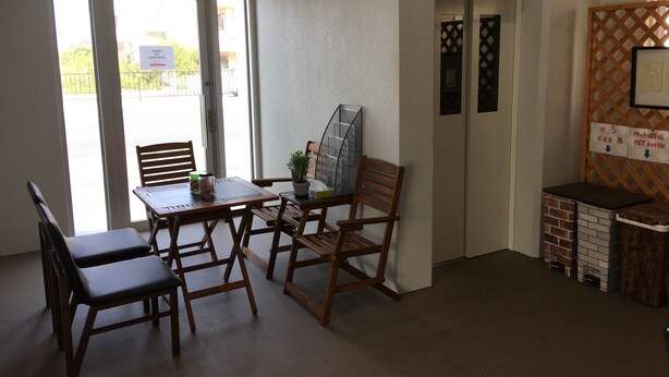 A room with a wooden table and chairs, a small potted plant, and a pet bottle sign. - Mr KINJO in Nishihara Inter (Ginowan)