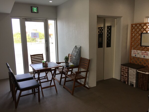 A room with a wooden table and chairs, a small potted plant, and a pet bottle sign. - Mr KINJO in Nishihara Inter (Ginowan)