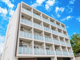 Un edificio de varios pisos con balcones, unidades de aire acondicionado y un cielo azul despejado.