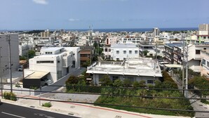 A cityscape with a mix of residential and commercial buildings, a clear sky, and a distant view of the sea. - Mr KINJO in Nishihara Inter (Ginowan)