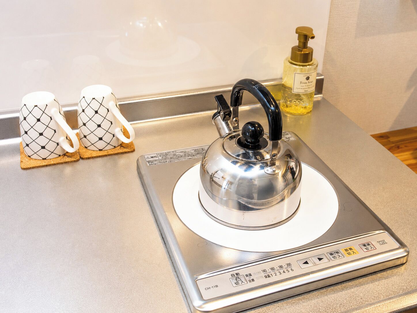 Une cuisine avec une bouilloire posée sur une balance, deux tasses et un distributeur de savon.