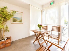 Un balcón con mesa y sillas de madera, una planta en maceta y un cuadro en la pared.