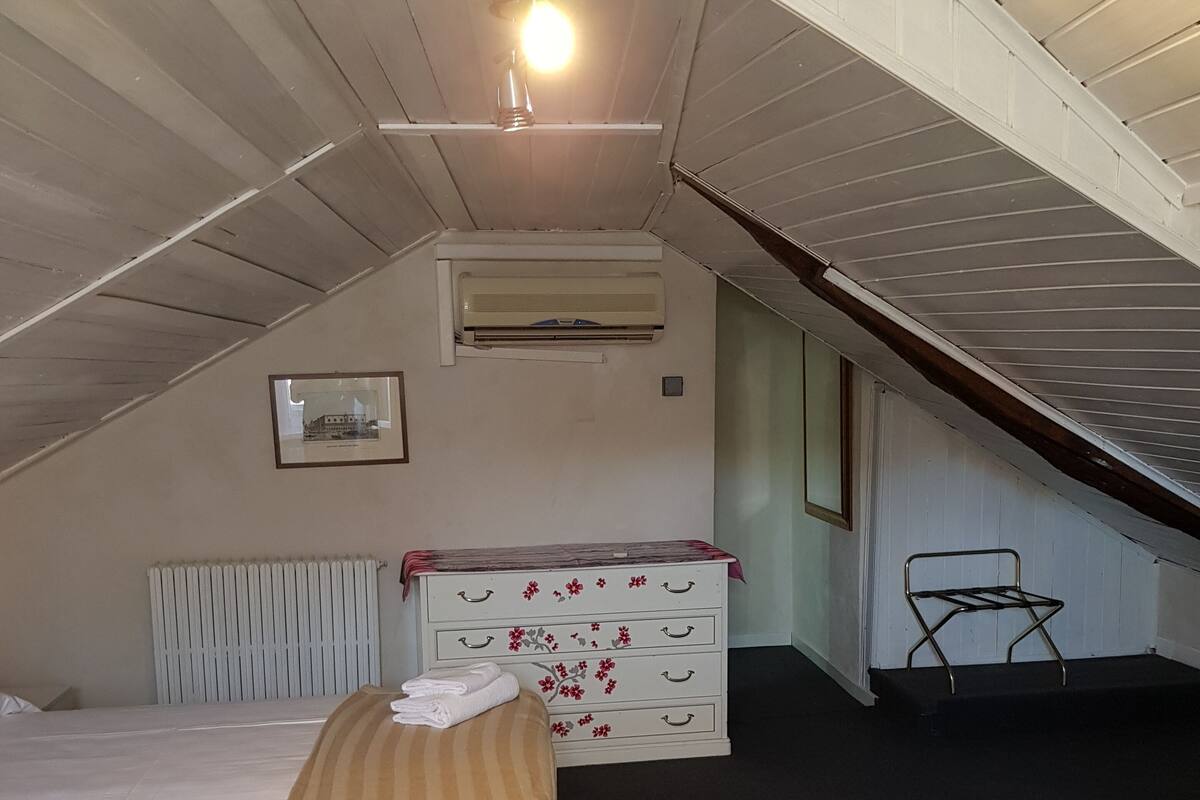 A bedroom with a bed, a dresser, a radiator, an air conditioning unit, and a staircase.
