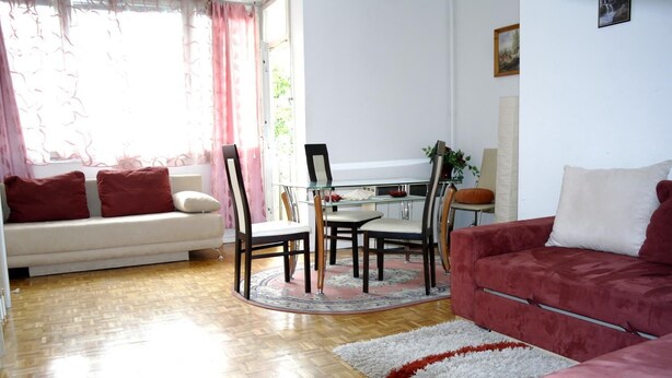 A living room with a sofa, a red couch, a dining table with chairs, and a window with curtains.