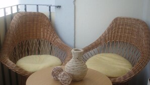 A balcony with two wicker chairs and a small round table, featuring a woven vase and decorative balls.