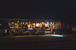 A well-lit outdoor dining area with a covered seating area and a visible entrance to a building.
