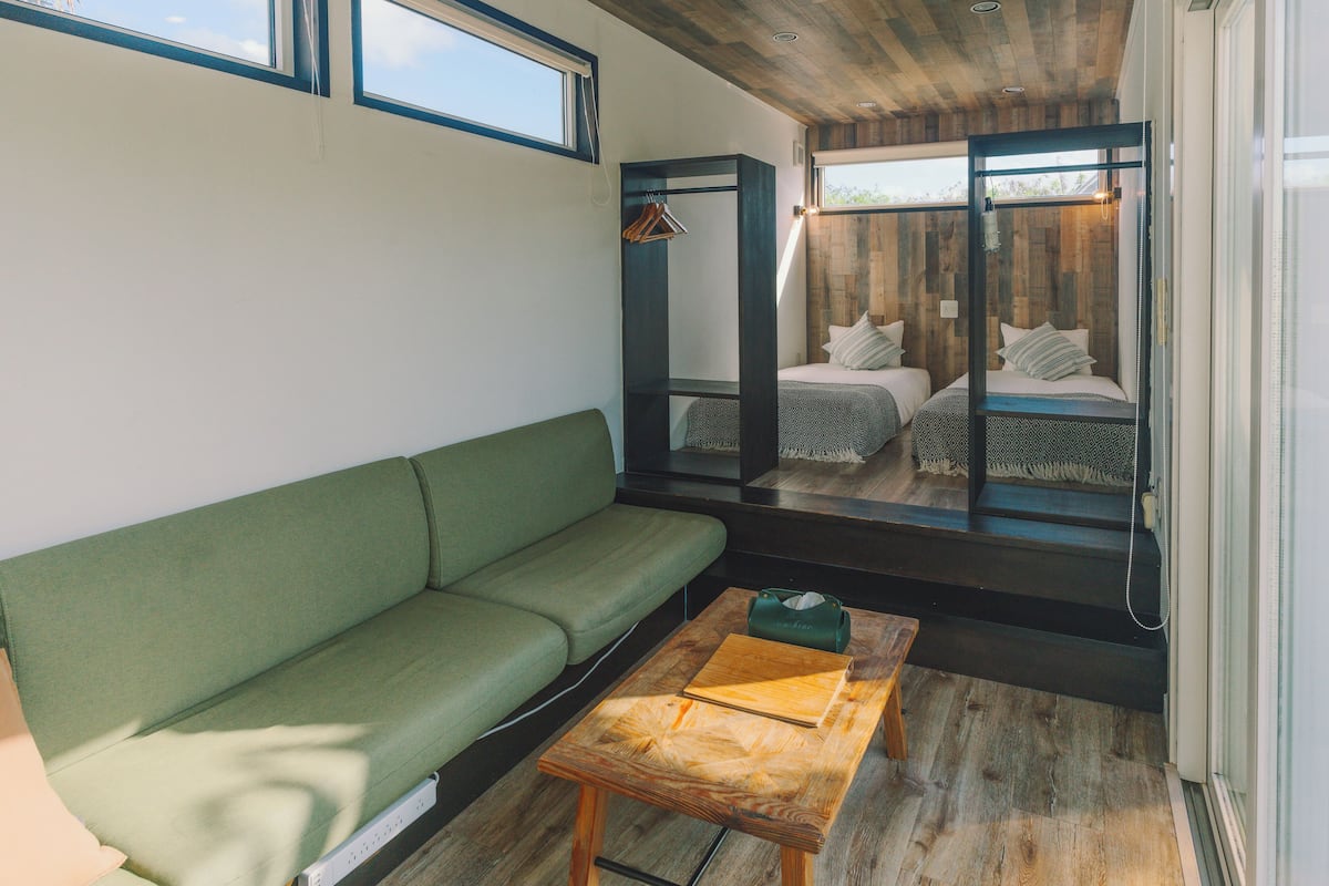 A modern, compact room with a green sofa, a wooden table, and a bed with a metal frame.