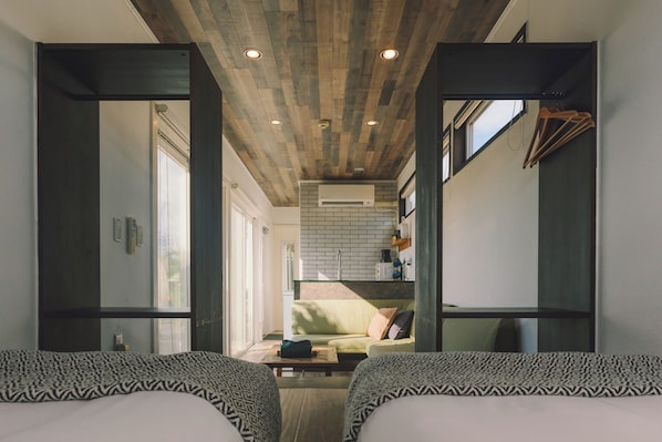 A modern hotel room with a wooden ceiling, a sofa, a bed, and a small kitchenette area.