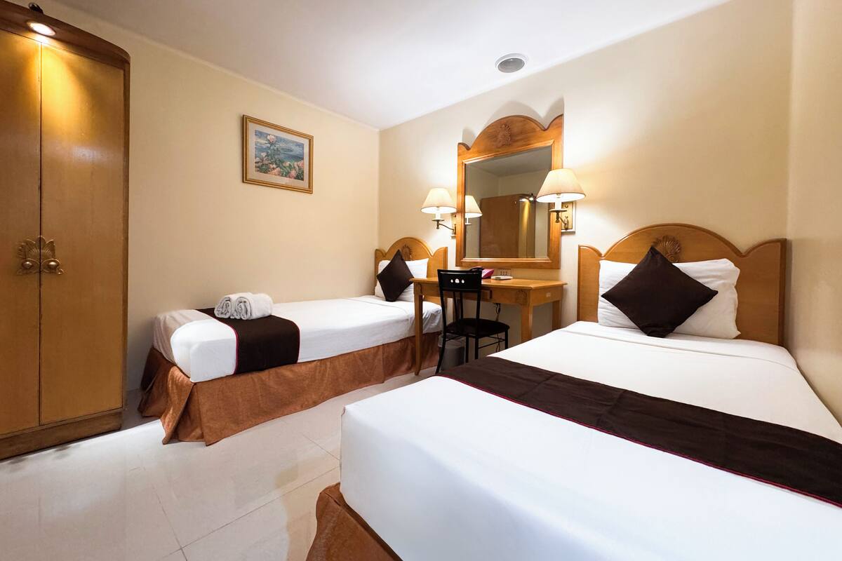 Une chambre d’hôtel avec deux lits simples, un bureau, une chaise, une armoire et un miroir.