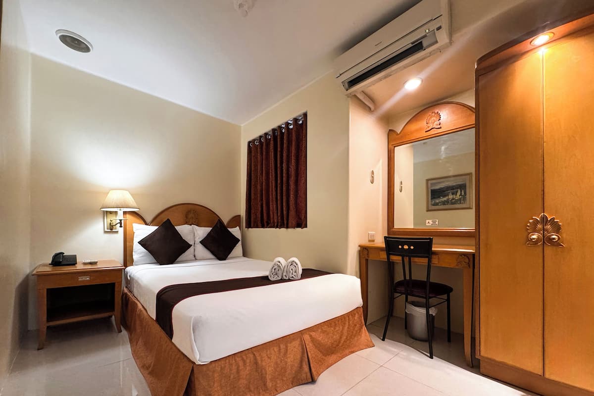 Une chambre d’hôtel comprenant un lit, un bureau, une chaise, une armoire, un miroir et une lampe.
