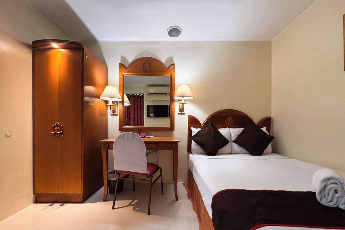 Une chambre d’hôtel équipée d’un lit, d’un bureau, d’une chaise, d’une armoire et de deux lampes fixées au mur.