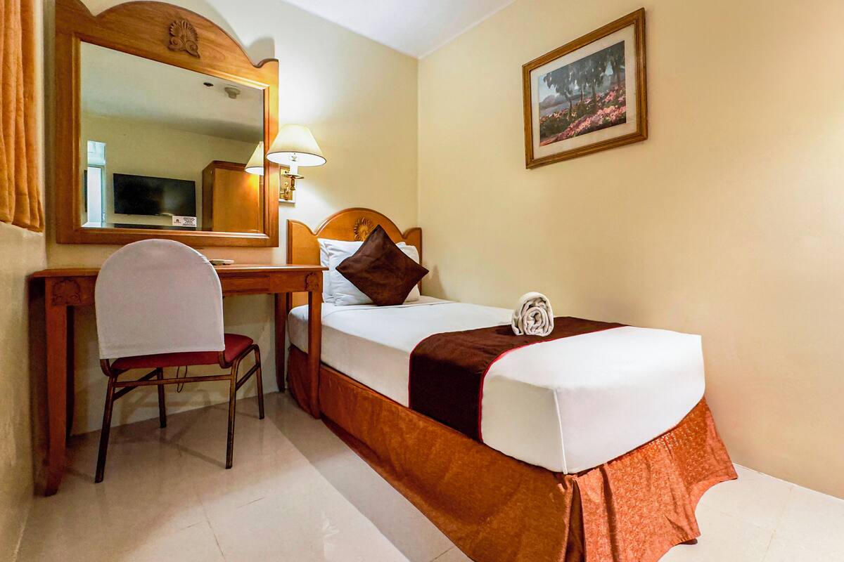 Une chambre d’hôtel avec un lit, un bureau, une chaise, un miroir, une lampe et un tableau au mur.