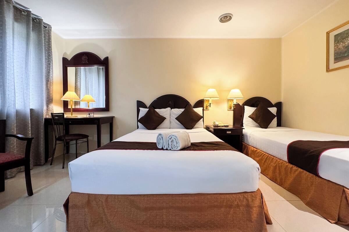 Une chambre d’hôtel avec deux lits simples, un bureau avec une chaise, un miroir et deux lampes de chevet.