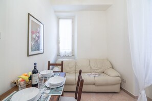 Un coin repas avec une table dressée pour deux personnes, un canapé, un tableau encadré et une bouteille de vin.