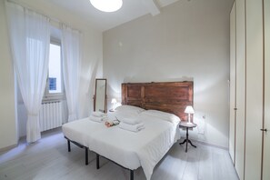 Une chambre à coucher avec un grand lit, des rideaux blancs, une tête de lit en bois, une table de chevet avec une lampe et un radiateur.