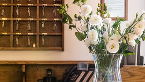 A reception desk with a wooden panel, a key rack, a phone, and a vase with white flowers. - Villa Rinascimento Dependance (Lucca)