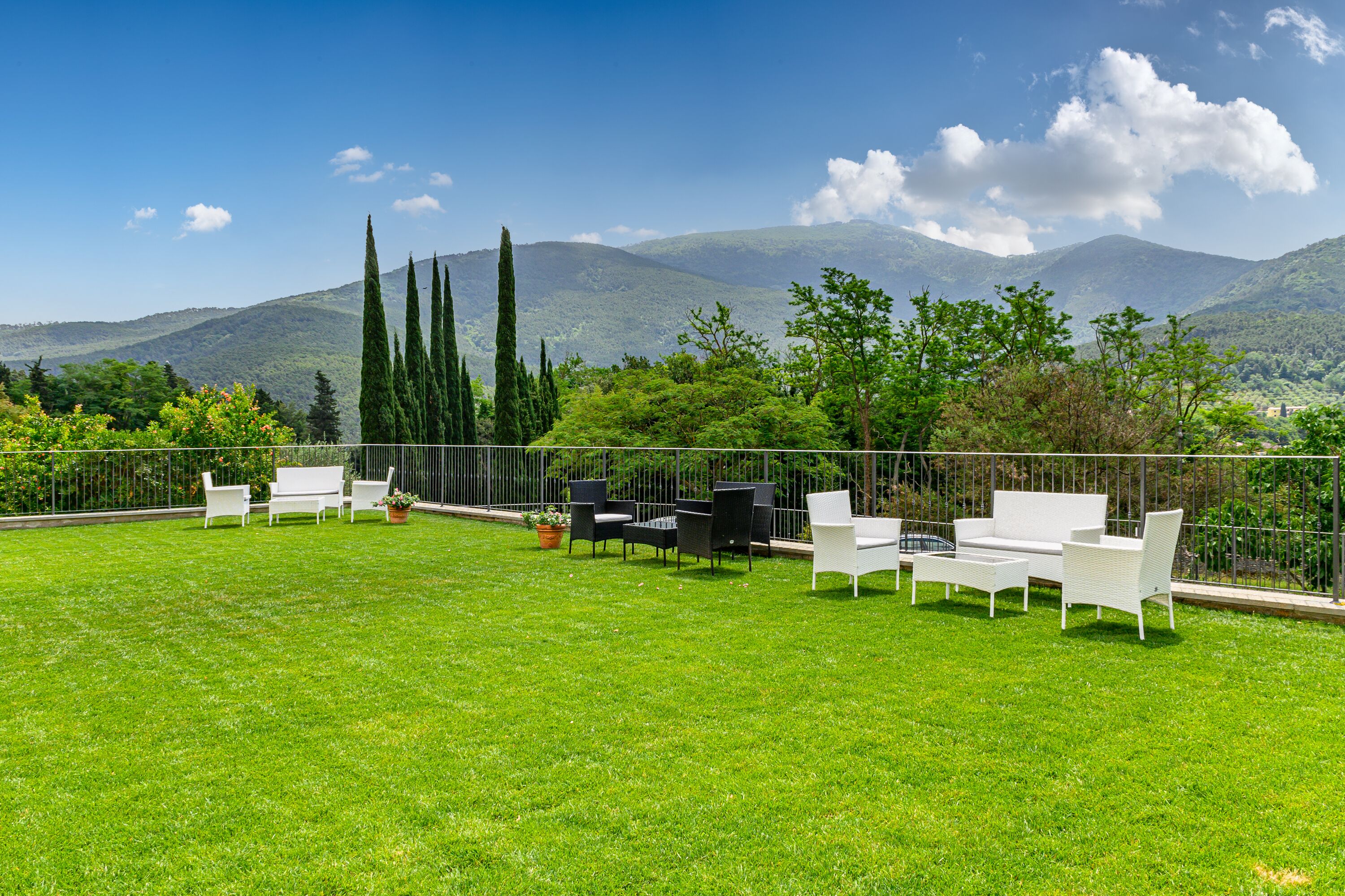 Un espacio al aire libre con césped, mobiliario blanco y vistas a montañas.