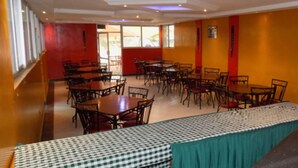 A dining area with multiple tables and chairs, a checkered tablecloth, and a view of the outside through large windows. - Shalom House - Hostel (Nairobi)