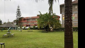 A grassy courtyard with picnic tables, a gazebo, and a palm tree. - Shalom House - Hostel (Nairobi)