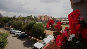 A view of a parking lot with several cars, a building in the background, and red flowers in the foreground. - Shalom House - Hostel (Nairobi)