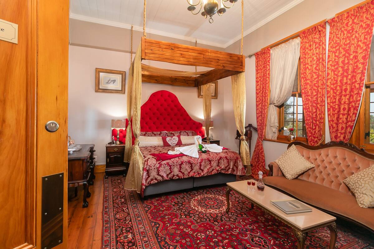 Een slaapkamer met een hemelbed, een bank, een bijzettafeltje en een kamerbreed tapijt met een patroon.