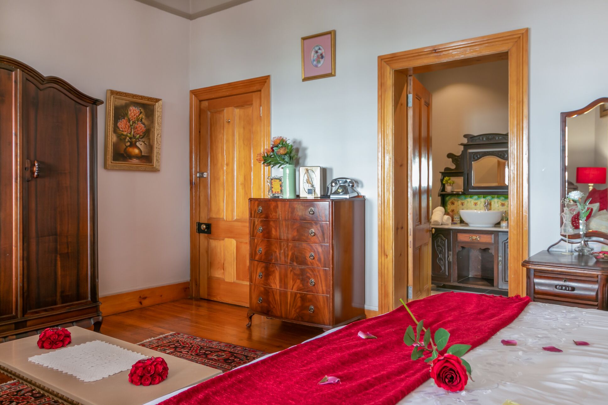 A bedroom with a bed, wooden dresser, and a bathroom visible through an open door.