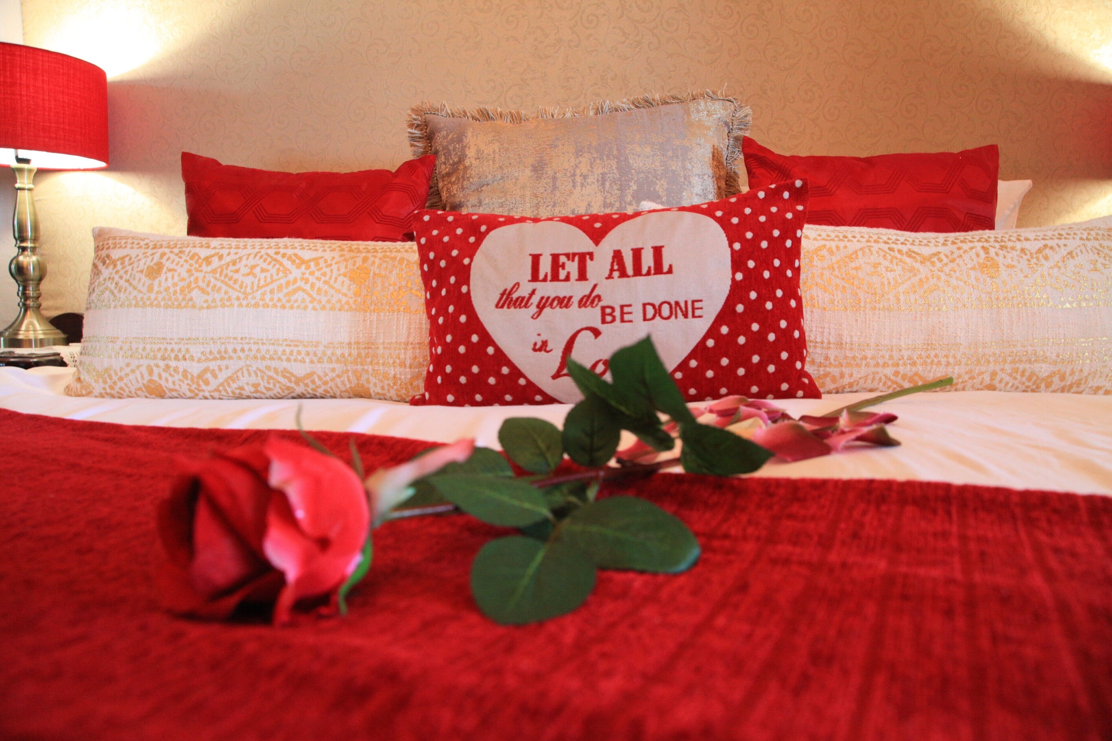 A bed with red bedding, a heart-shaped pillow with a motivational quote, and a red rose.