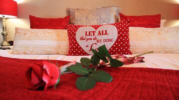 A bed with red bedding, a heart-shaped pillow with a motivational quote, and a red rose.