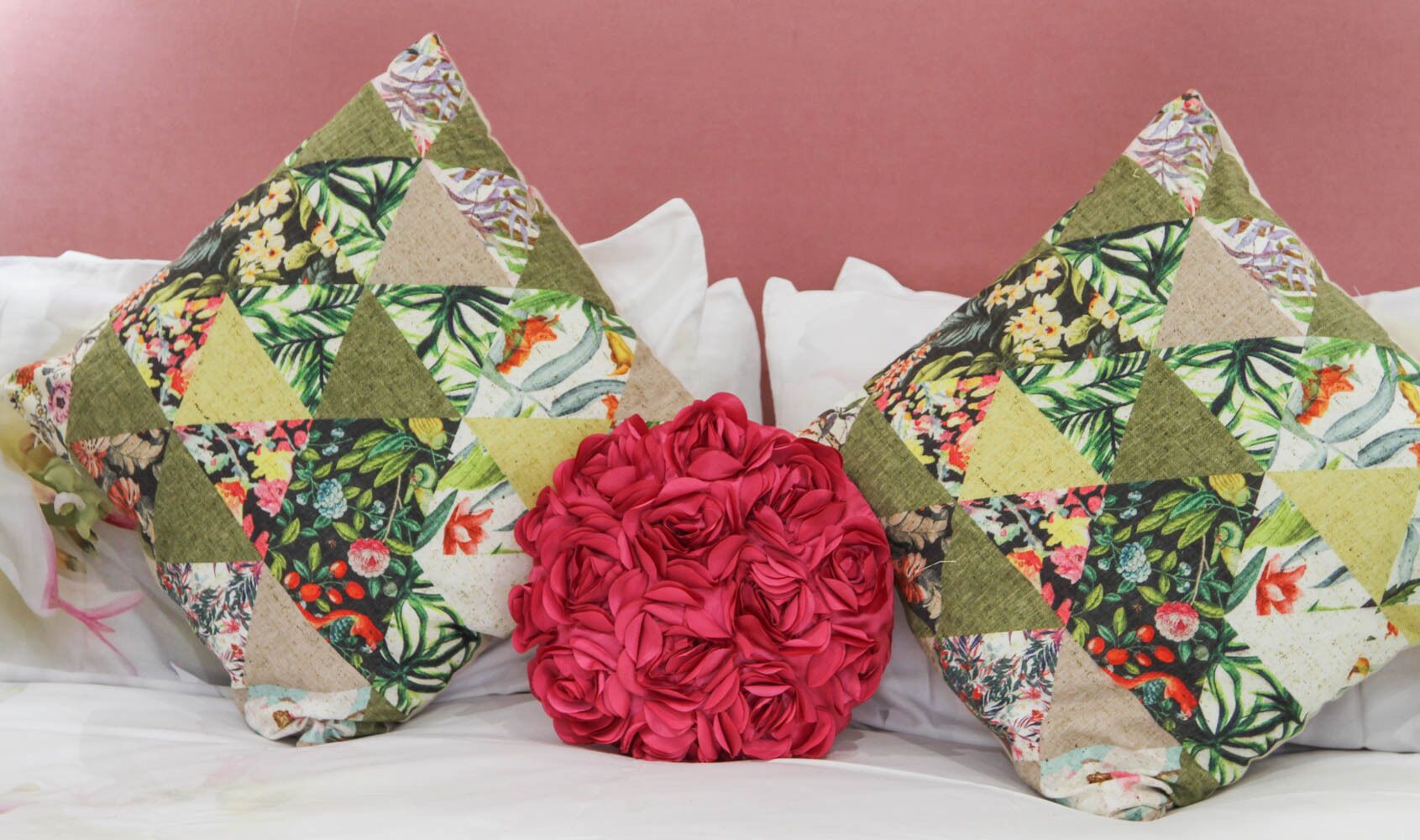 Two decorative pillows with floral patterns and a large red rose centerpiece on a bed.