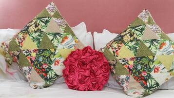 Two decorative pillows with floral patterns and a large red rose centerpiece on a bed.