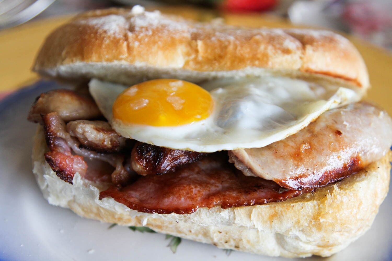 Un sándwich de desayuno con tocino, salchicha y un huevo frito en un pan.