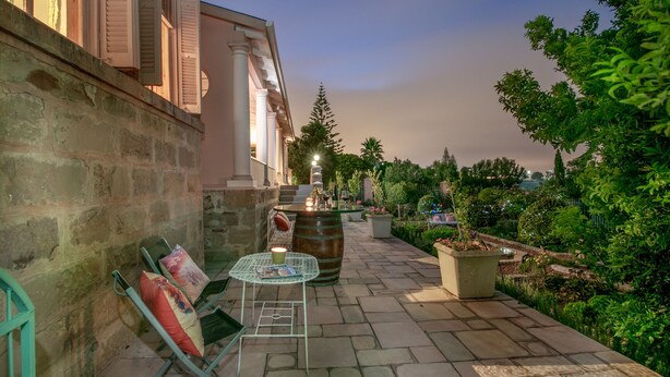 A stone-paved outdoor area with a table and chairs, a barrel, and potted plants. - Bettys Boutique Hotel (Mossel Bay)