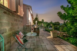 A stone-paved outdoor area with a table and chairs, a barrel, and potted plants.